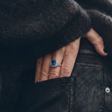 A high-end studio shot of the Azure Magma Signet ring, featuring a vibrant blue gemstone set in a handcrafted, rocky-textured 925 silver frame on volcanic sand.