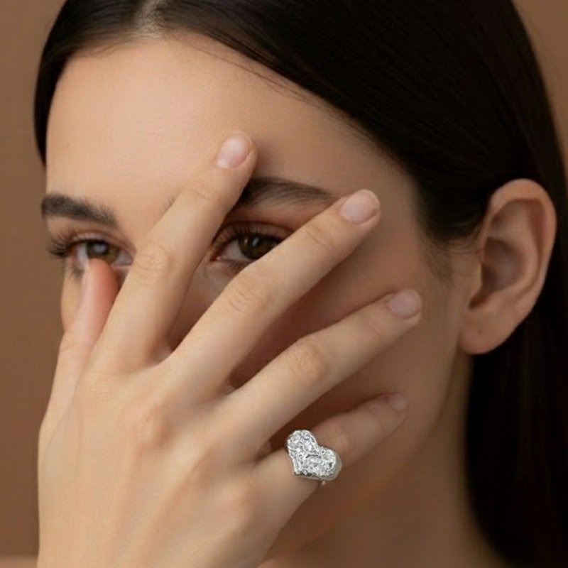 A handcrafted 925 sterling silver chevalier ring with a sculptural heart shape and raw texture, displayed on elegant dark green silk fabric