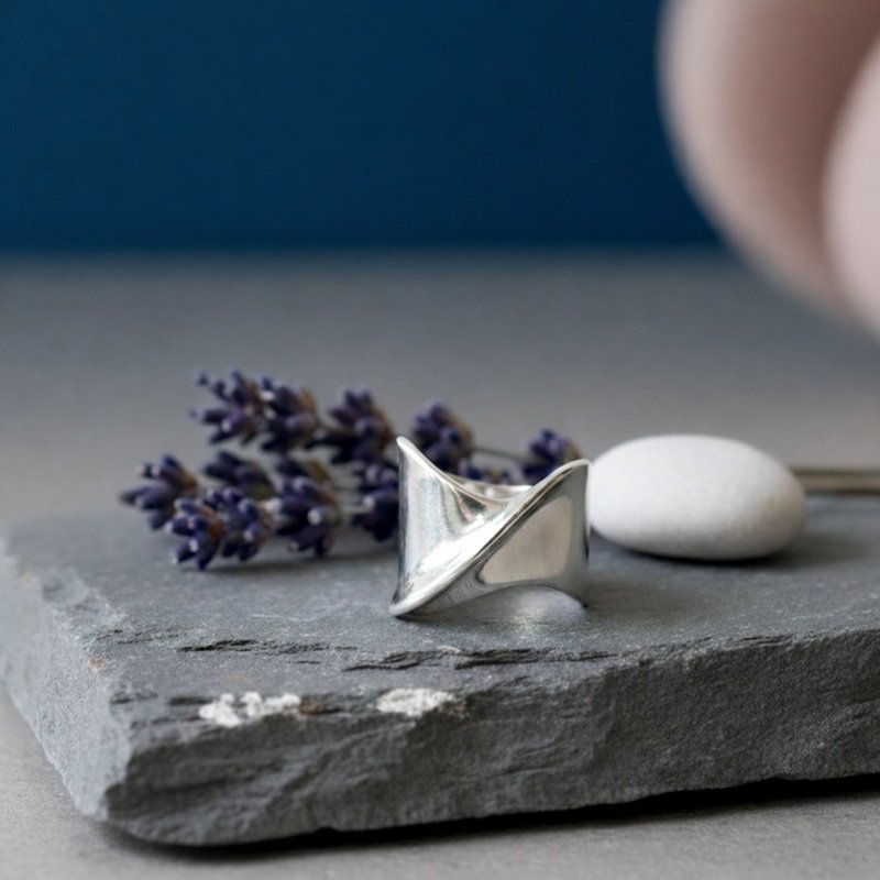 Handmade sterling silver 925 ring with a modern sculptural twist design, displayed on a natural grey stone with lavender