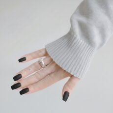 A woman with black matte nails and a grey knit sweater wearing the handcrafted Queens Regal Silver Ring, showcasing its bold sculptural ridges in a minimalist lifestyle setting